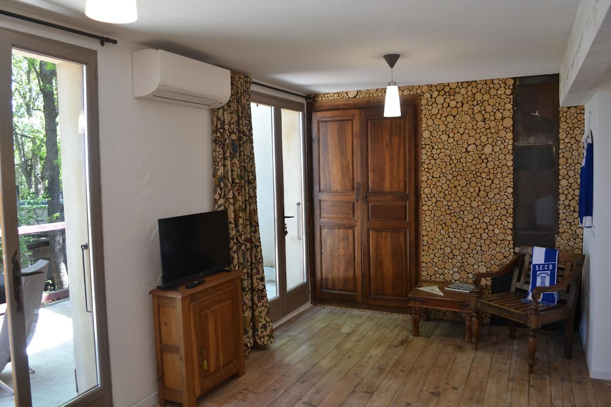 A room with a television on a wooden cabinet, a wooden chair, a table, and a wall with a log pattern.