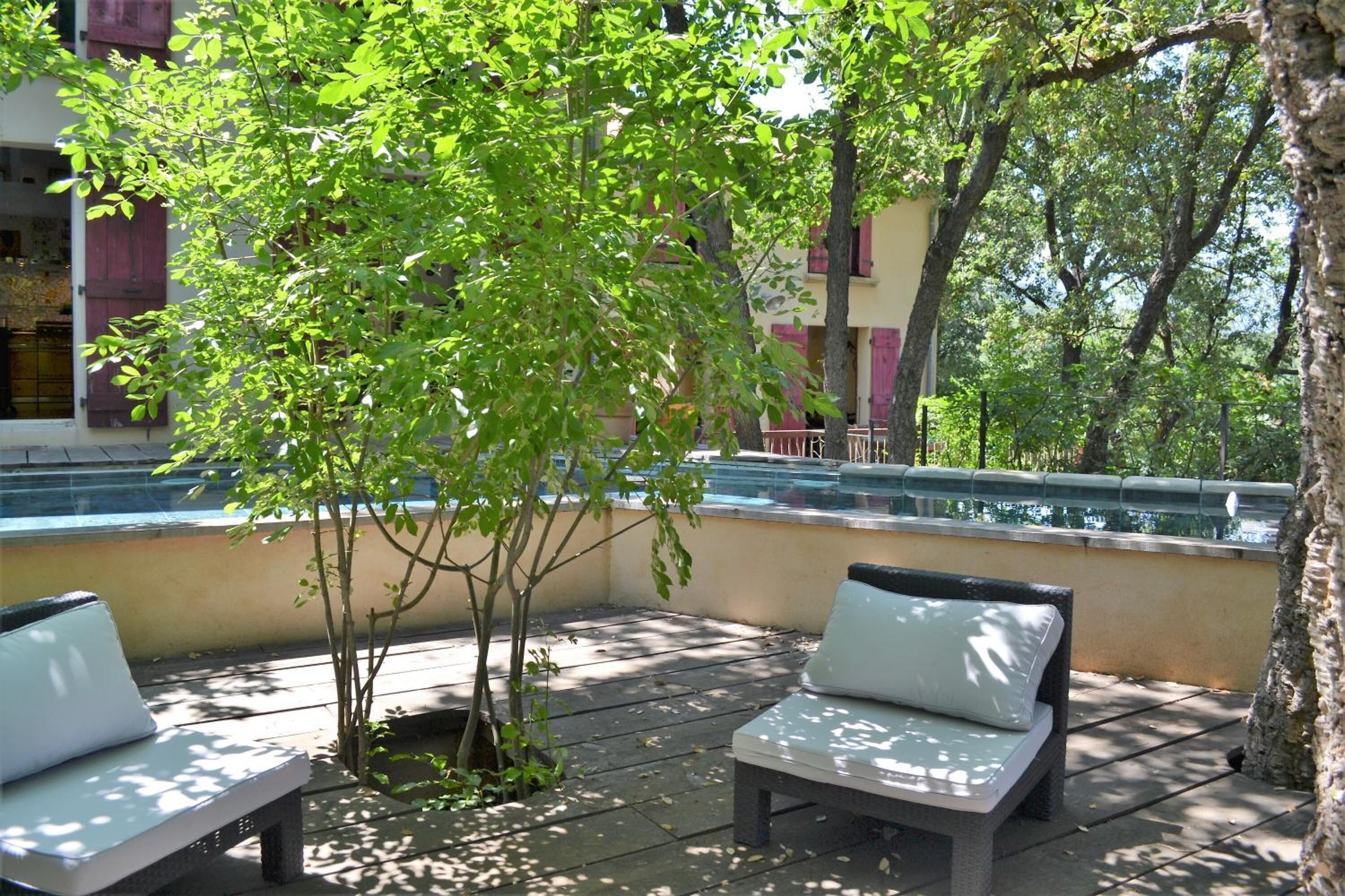 Ein Sitzbereich im Freien mit zwei weißen Sitzgelegenheiten, einem kleinen Baum und einem Pool im Hintergrund.