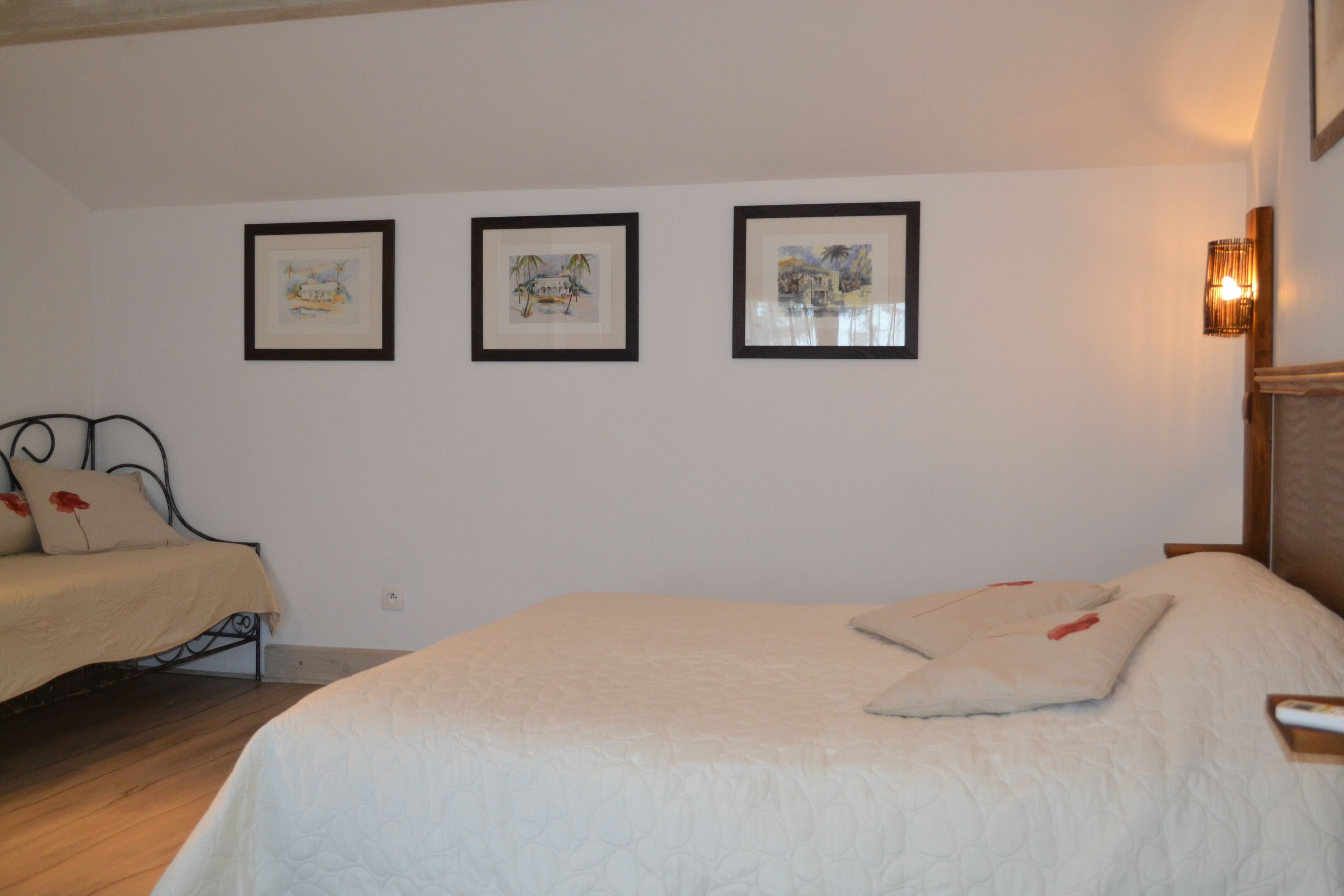 Ein Schlafzimmer mit einem Bett, einem zusätzlichen Bett und einem Nachttisch. An der Wand hängen drei Bilder in Rahmen.