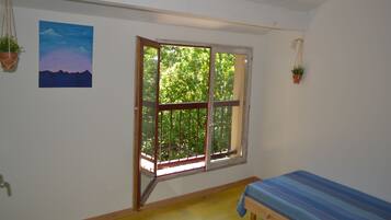 Una habitación con una cama, un ventanal con vista a árboles y un cuadro en la pared.