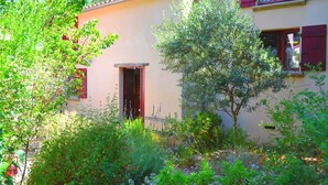 Una casa con jardín, puerta roja y ventana con contraventanas rojas.