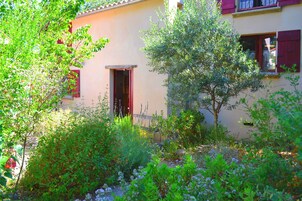 Uma casa com jardim, porta vermelha e janelas com contraportas vermelhas.