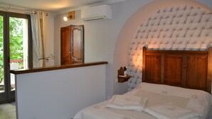 Un dormitorio con cama, cabecera arqueada, mesita de noche, espejo y ventana con cortinas.