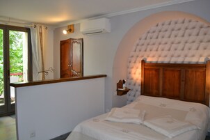 Quarto com cama, cabeceira em arco, mesa de cabeceira, espelho e janela com cortinas.