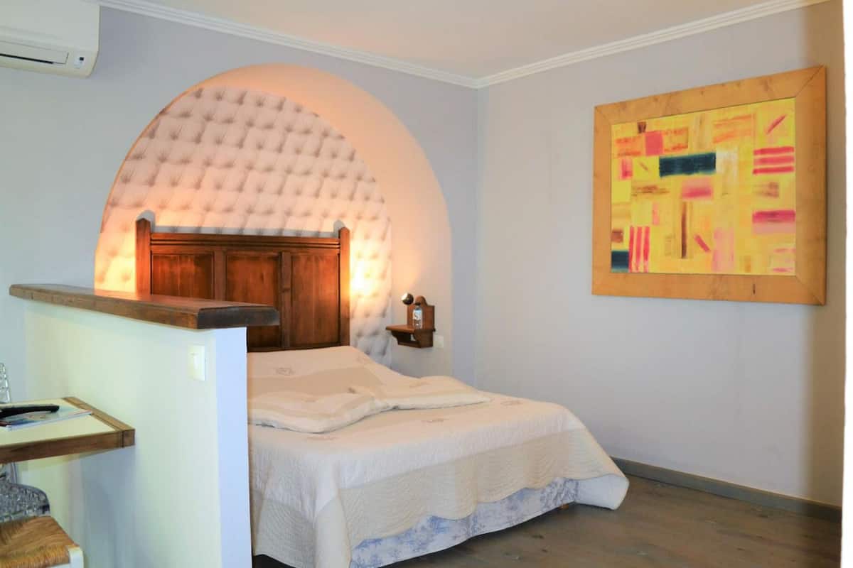 A bedroom with a bed, a wooden headboard, a wall-mounted artwork, and a small bedside table with a lamp.