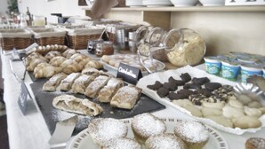 A buffet with various pastries and desserts, including cannoli and chocolate-covered items, displayed on a table with a sign indicating 'Ciacchino'.