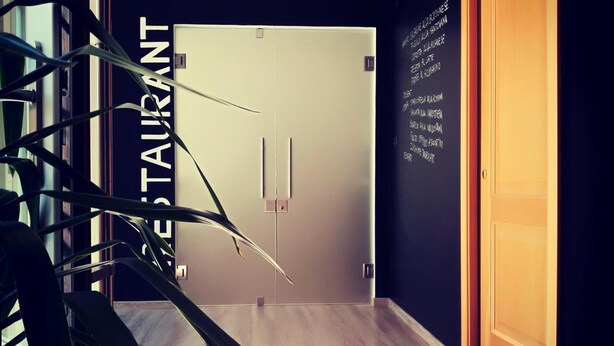 A modern interior with a wooden floor, a black wall with a white door, and a sign reading "RESTAURANT".