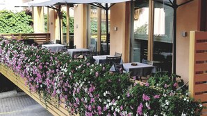 An outdoor seating area with tables and umbrellas, surrounded by flowering plants.