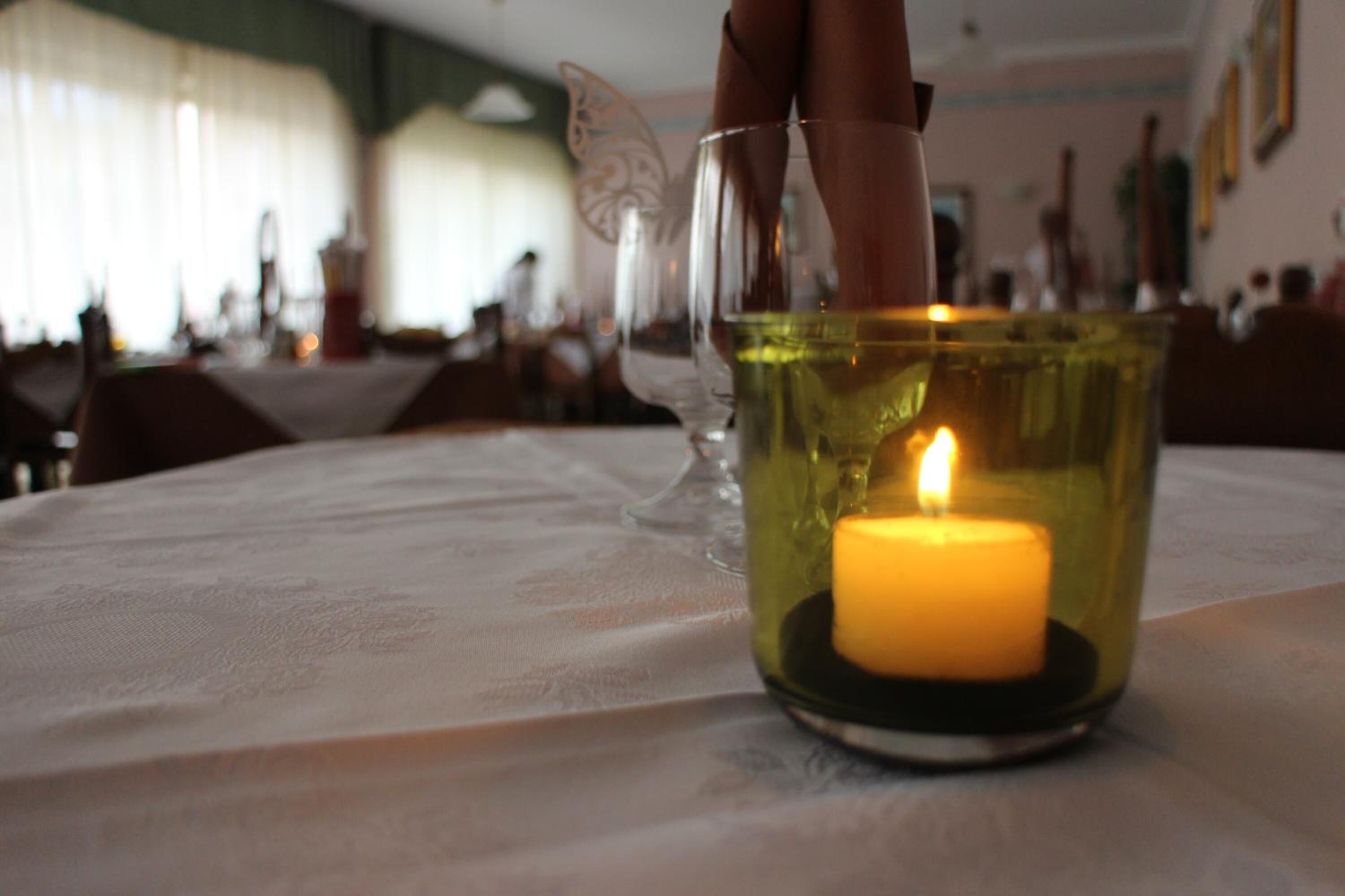 A candle in a glass holder on a table with a white tablecloth.