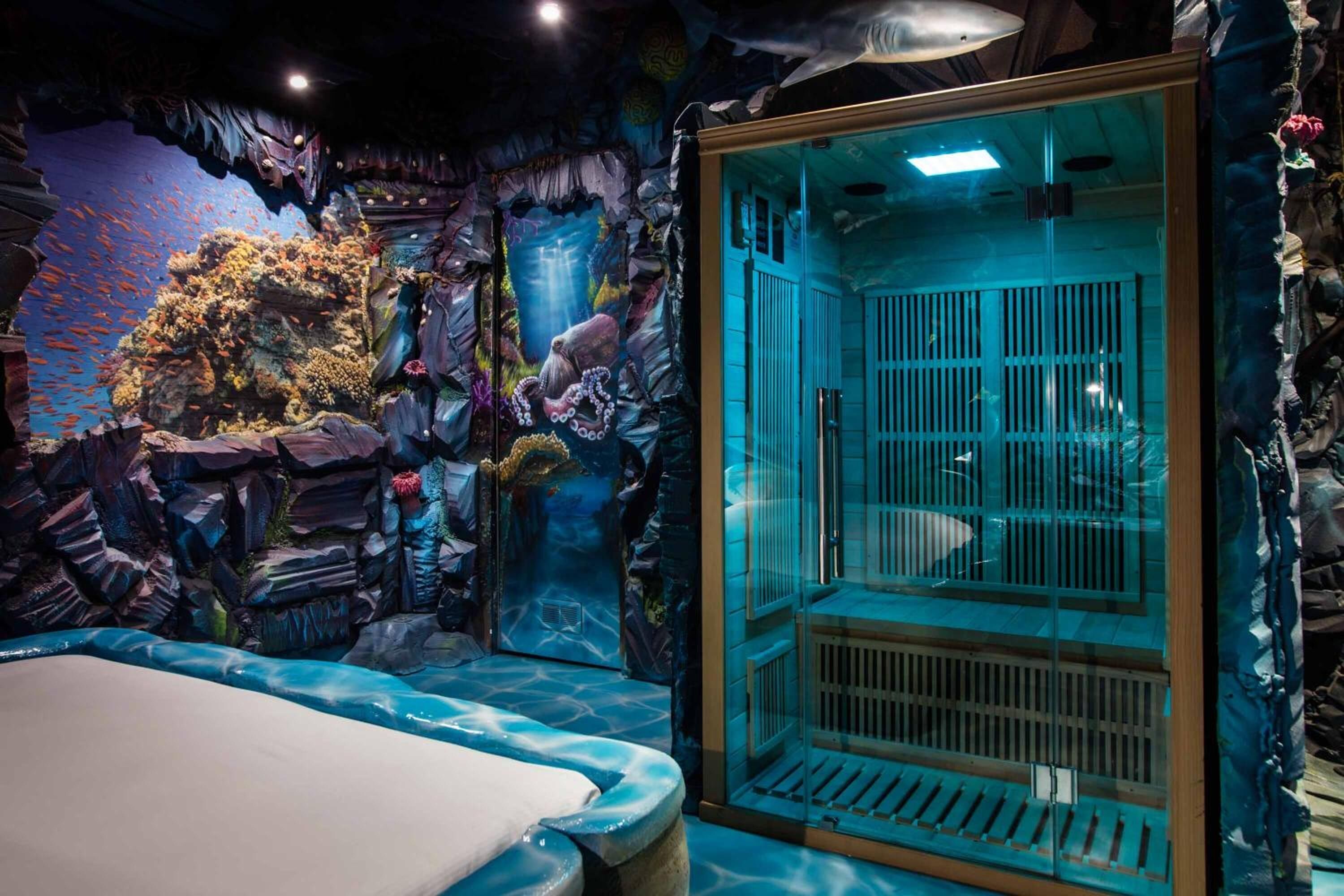 An underwater-themed room with a glass enclosure, a bed, and a rocky wall with marine decorations.