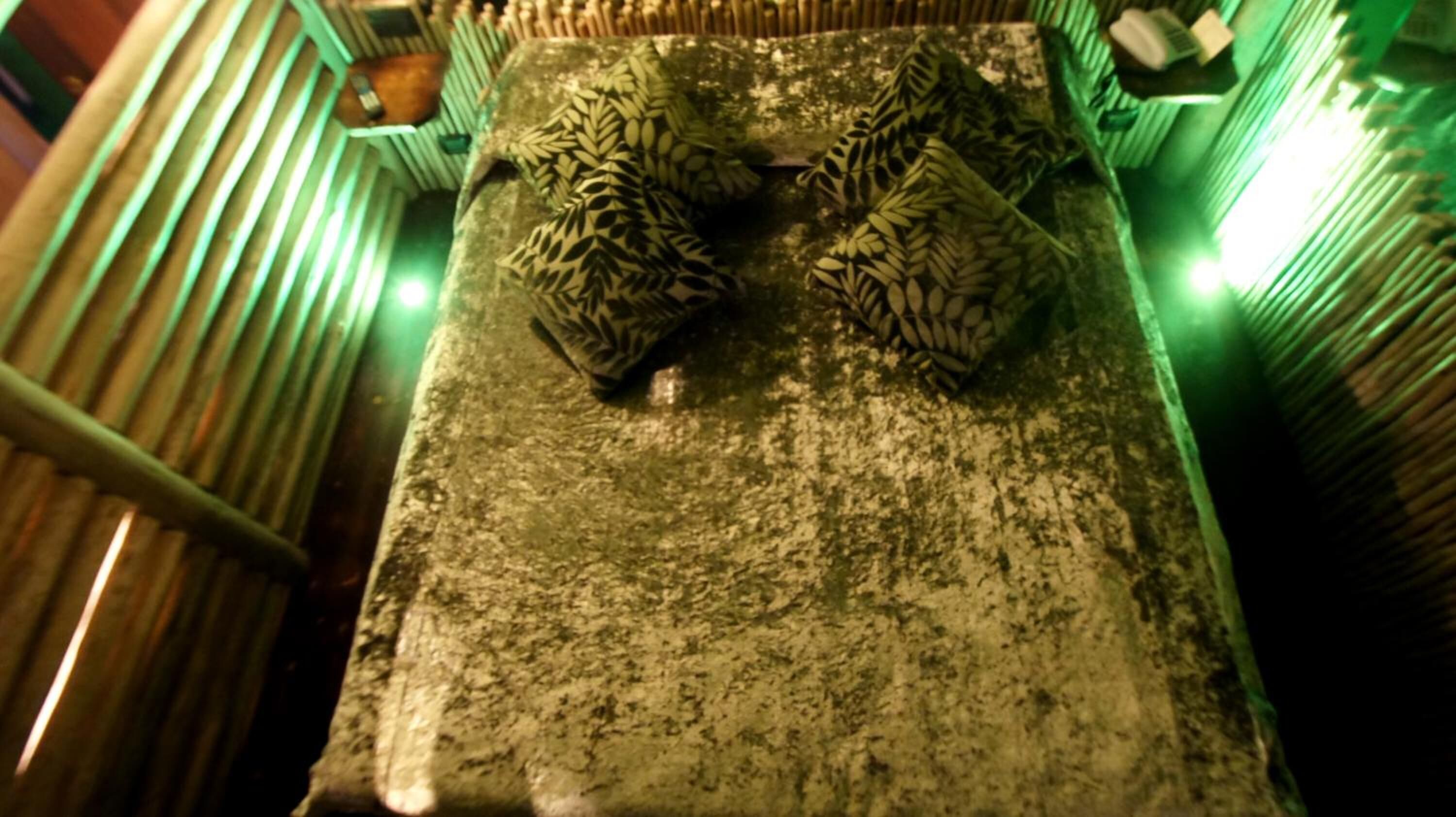 A room with a textured floor, a bed with patterned bedding, and a green-lit wall.