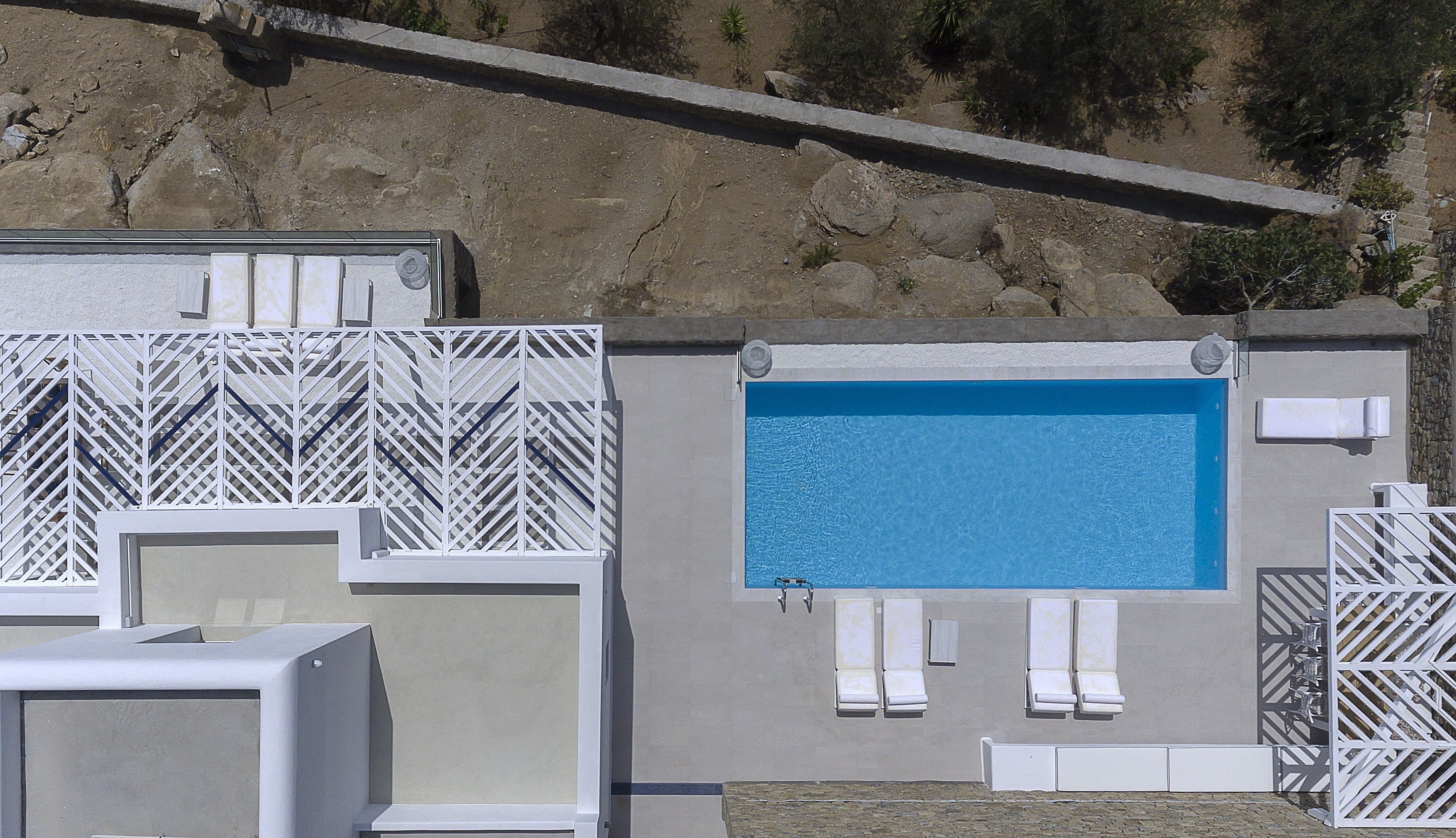 Zona de piscina con una pileta rectangular, sillas de descanso blancas y una cerca de celosía blanca.