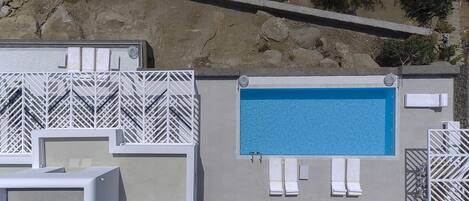 A pool area with a rectangular pool, white lounge chairs, and a white lattice fence.