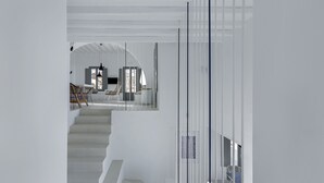 A modern interior with a staircase leading to a second floor, a seating area with chairs, and a view of the outdoors. - Sealine Villas (Mykonos)