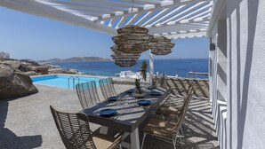A terrace with a pool, dining table set for four, and wicker chairs. - Sealine Villas (Mykonos)