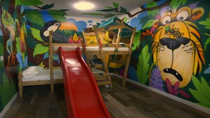 A children's playroom with a wooden bunk bed, a red slide, and a mural of jungle animals. - Apartamentos El Volante II (Ciempozuelos)