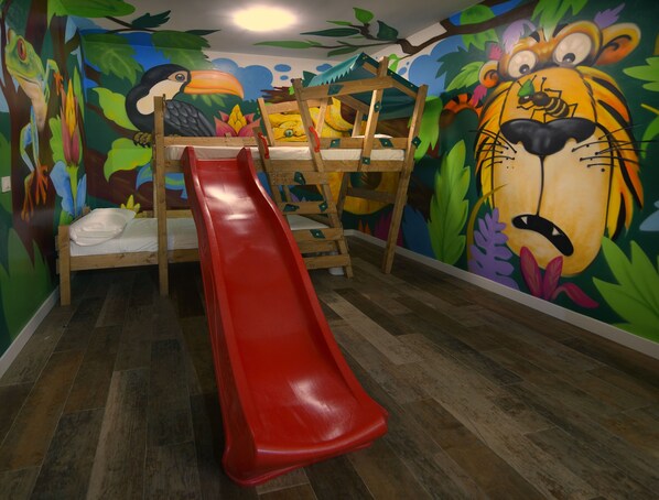 A children's playroom with a wooden bunk bed, a red slide, and a mural of jungle animals. - Apartamentos El Volante II (Ciempozuelos)