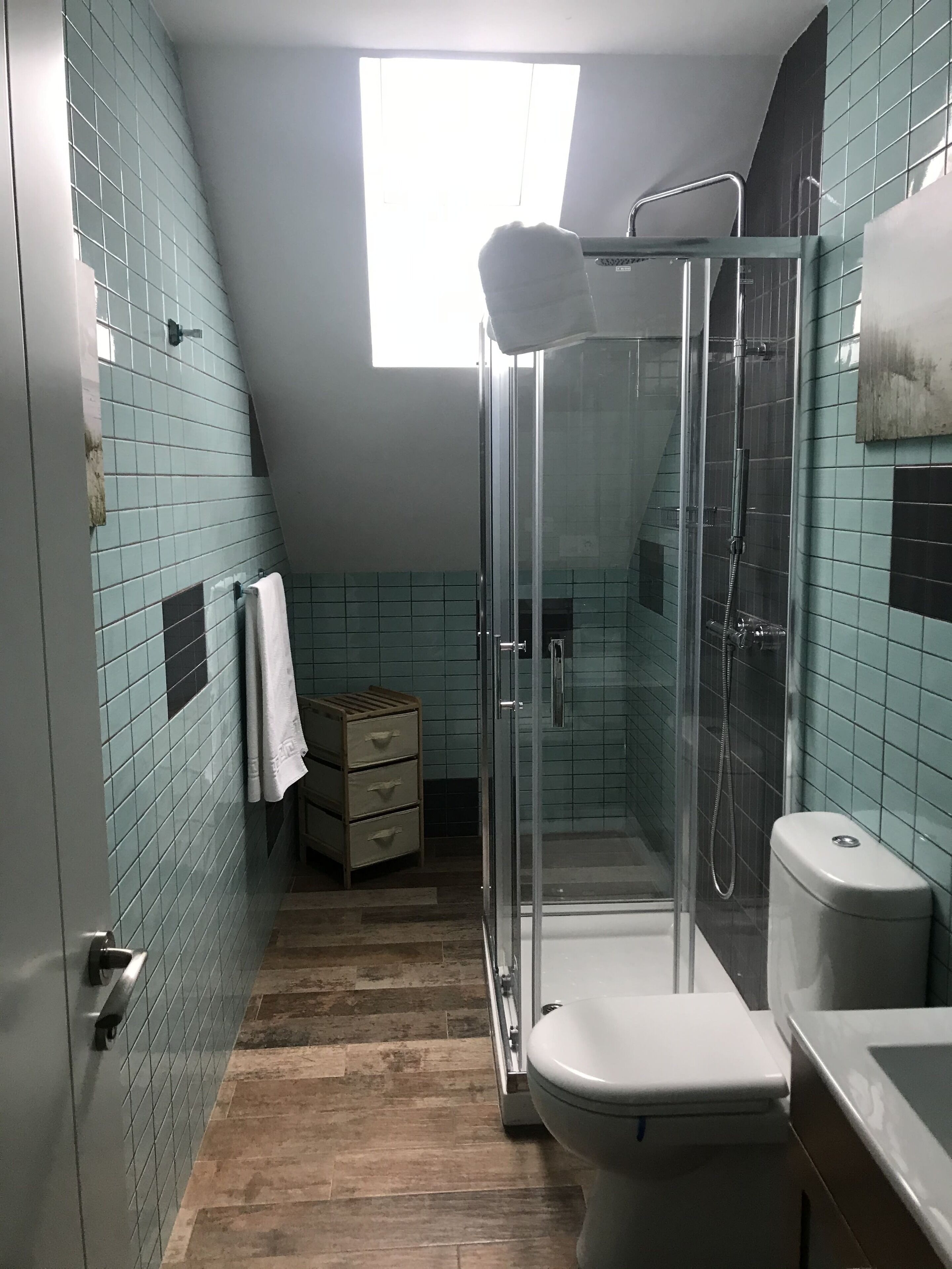 A bathroom with a glass-enclosed shower, a toilet, and a small wooden cabinet.