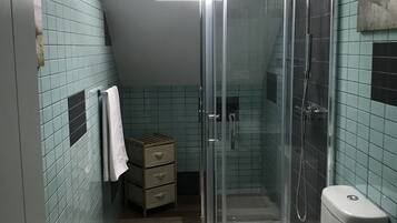 A bathroom with a glass-enclosed shower, a toilet, and a small wooden cabinet.