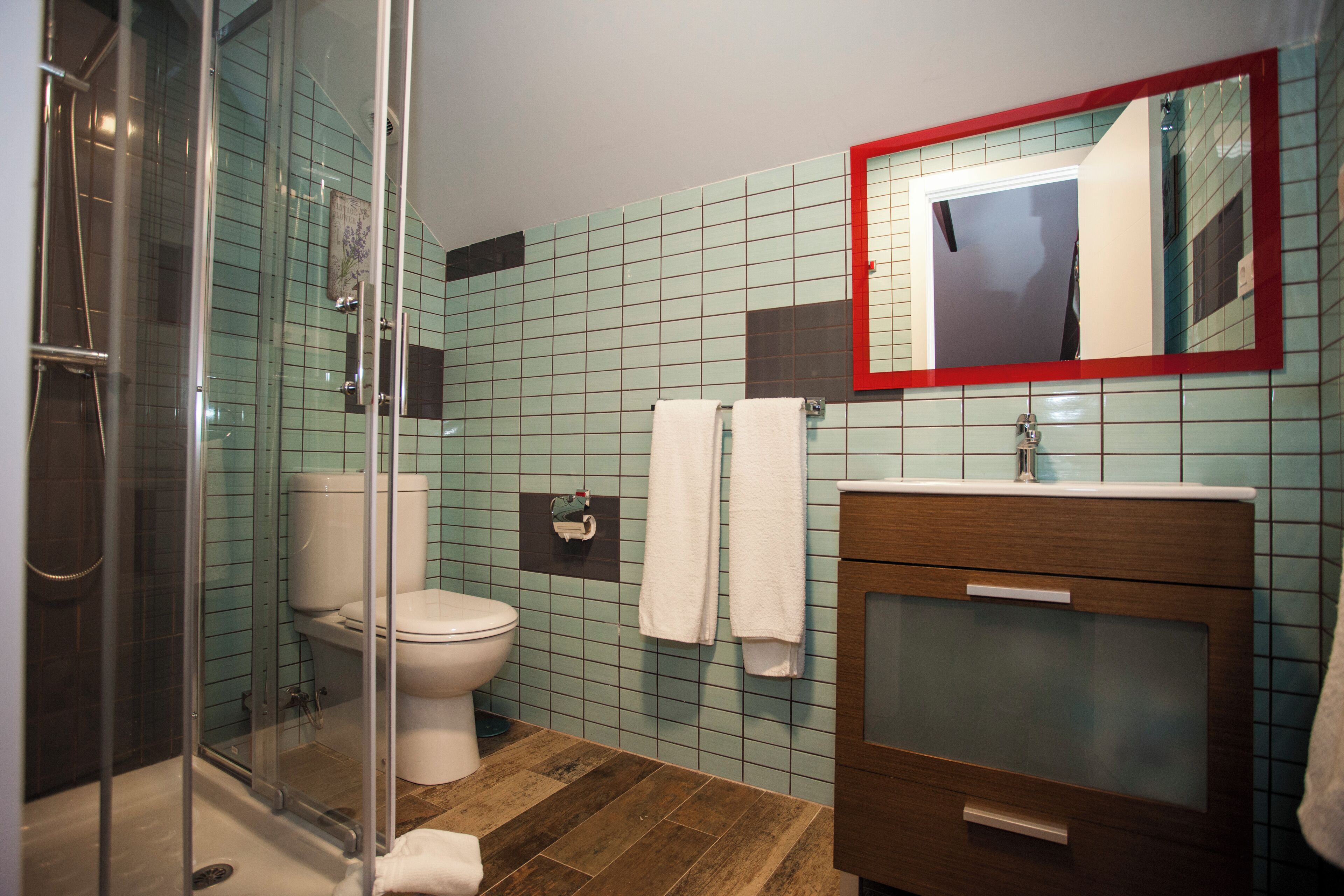 Un baño con cabina de ducha de vidrio, inodoro, lavamanos con espejo y paredes con azulejos.