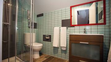 Un baño con cabina de ducha de vidrio, inodoro, lavamanos con espejo y paredes con azulejos.