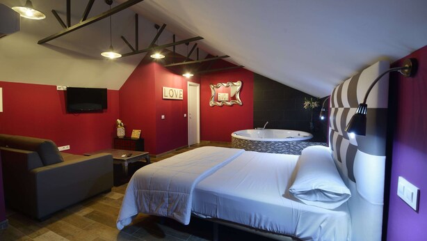 A bedroom with a bed, a sofa, a small table, a TV, a mirror, and a bathroom with a bathtub. - Apartamentos El Volante II (Ciempozuelos)