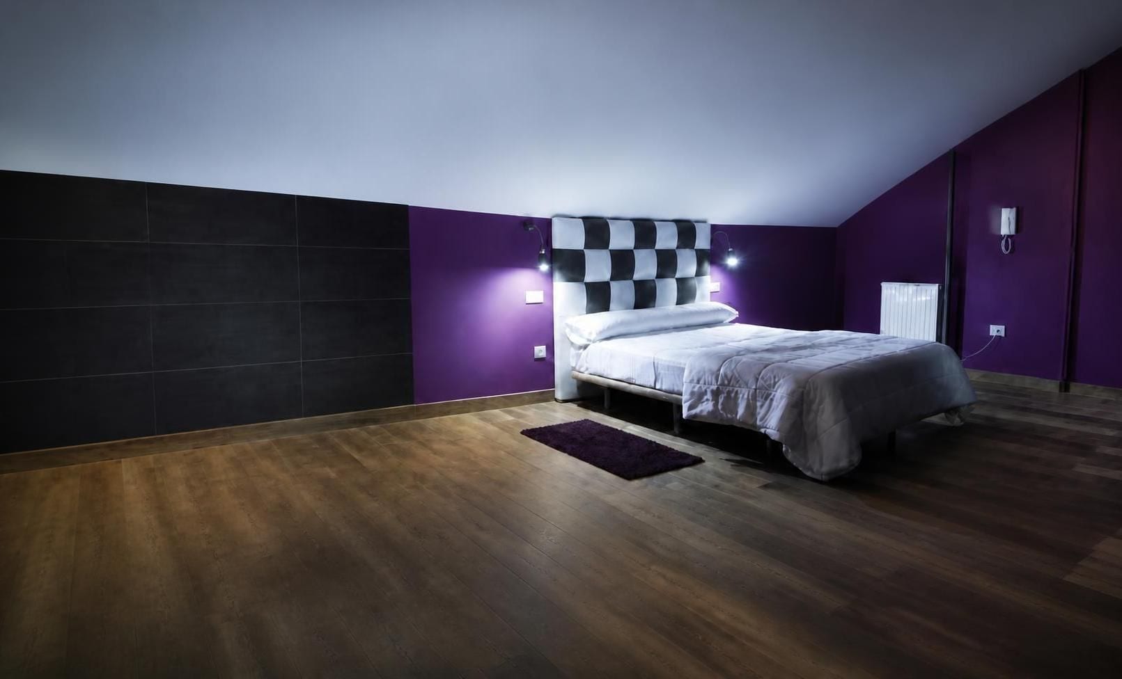 Une chambre à coucher avec un lit, une tête de lit à carreaux, des murs violets et un plancher en bois.
