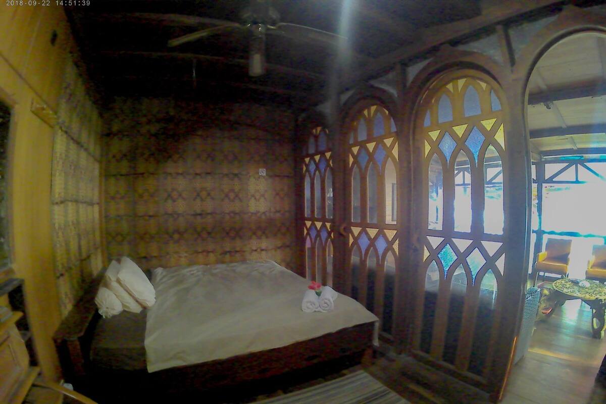 Un dormitorio con cama, marcos de ventana de madera y vistas al exterior.