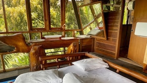 Una cabaña de madera con una cama, una silla y una ventana con vistas a la vegetación.