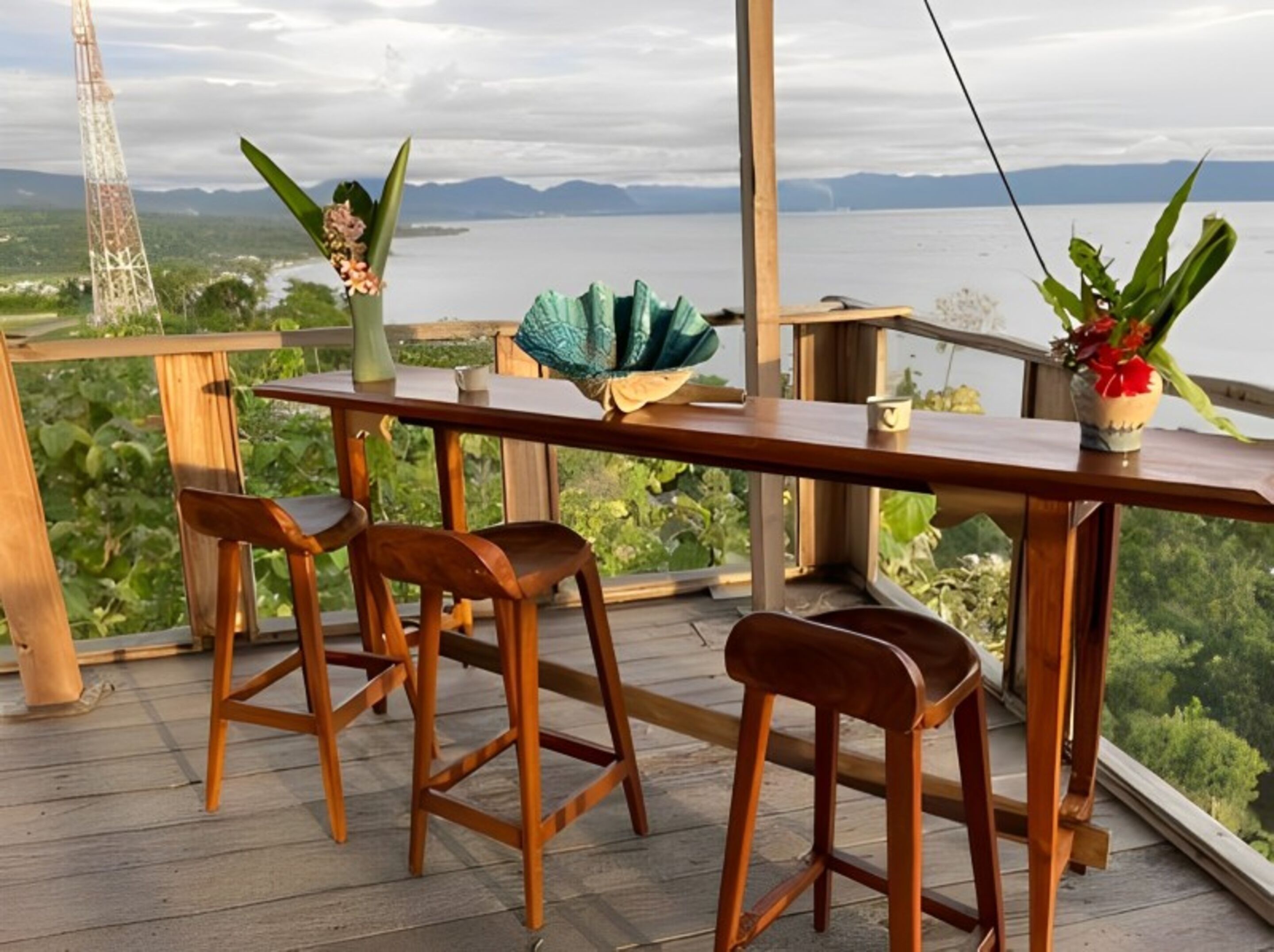 Une terrasse en bois avec une table et des chaises, offrant une vue panoramique sur les montagnes et un plan d’eau.
