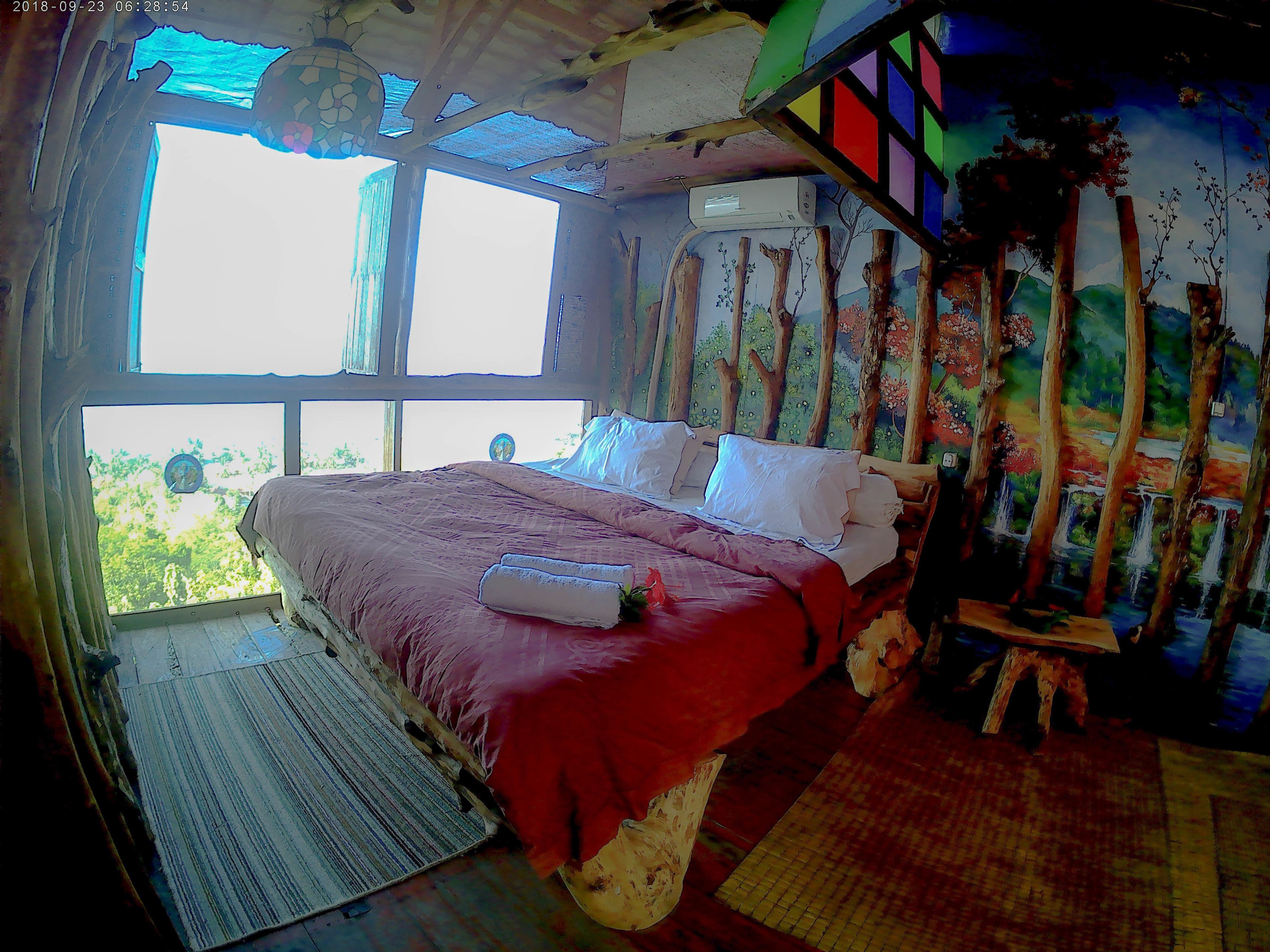 A bedroom with a large bed, a window, and a mural on the wall.