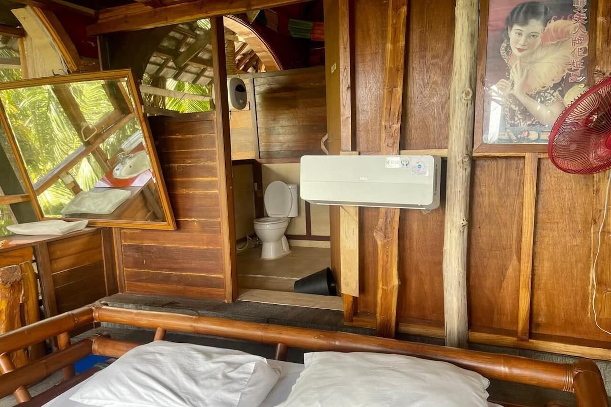 Una habitación de madera con una cama, un espejo, un inodoro y un aire acondicionado instalado en la pared.