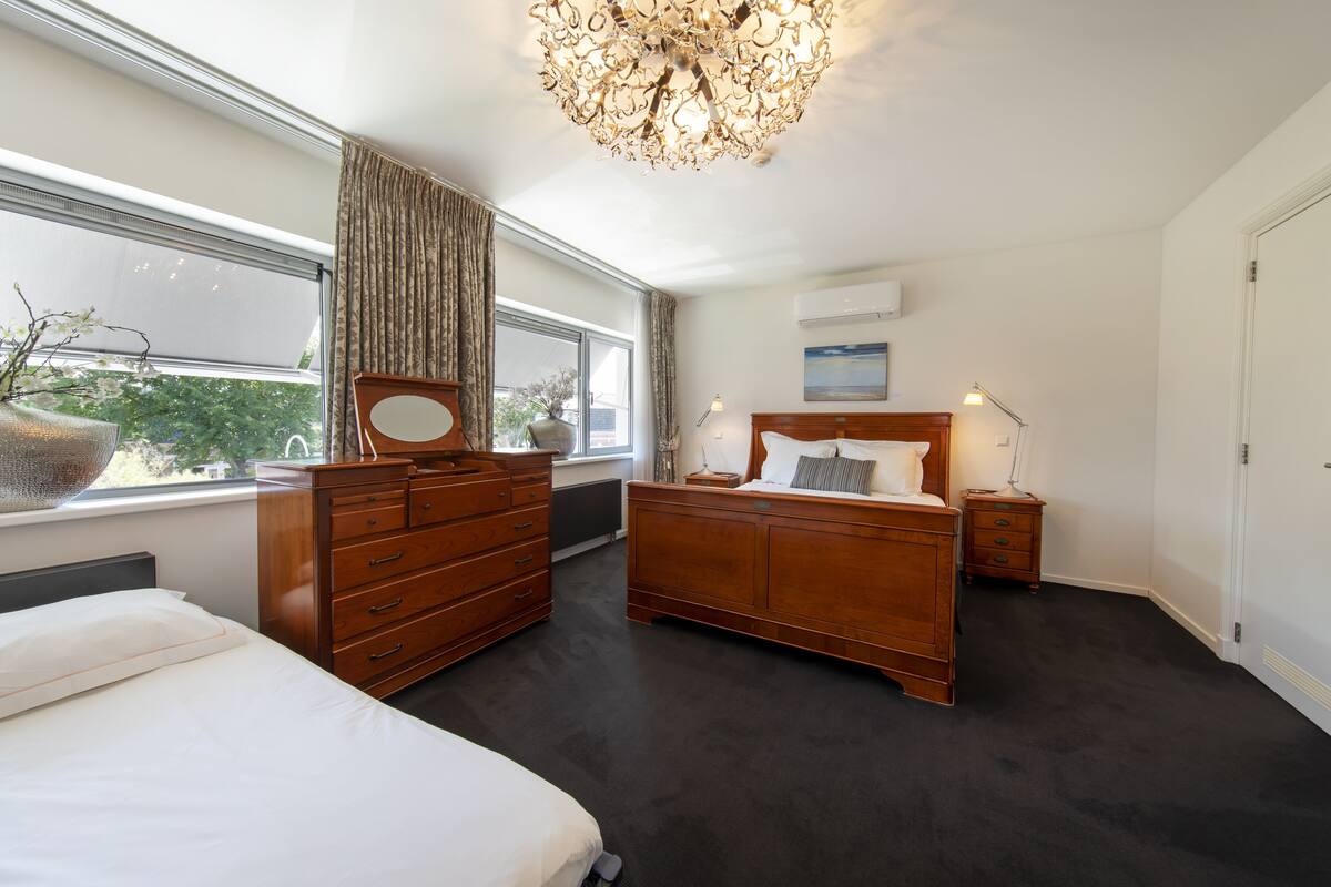 A bedroom with a large bed, a dresser, a nightstand, and a chandelier.
