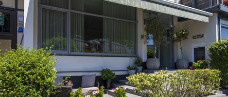 A hotel with a covered outdoor seating area, large windows, and potted plants.