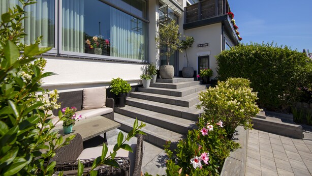 A modern building with a large window, outdoor seating area, and steps leading to the entrance.