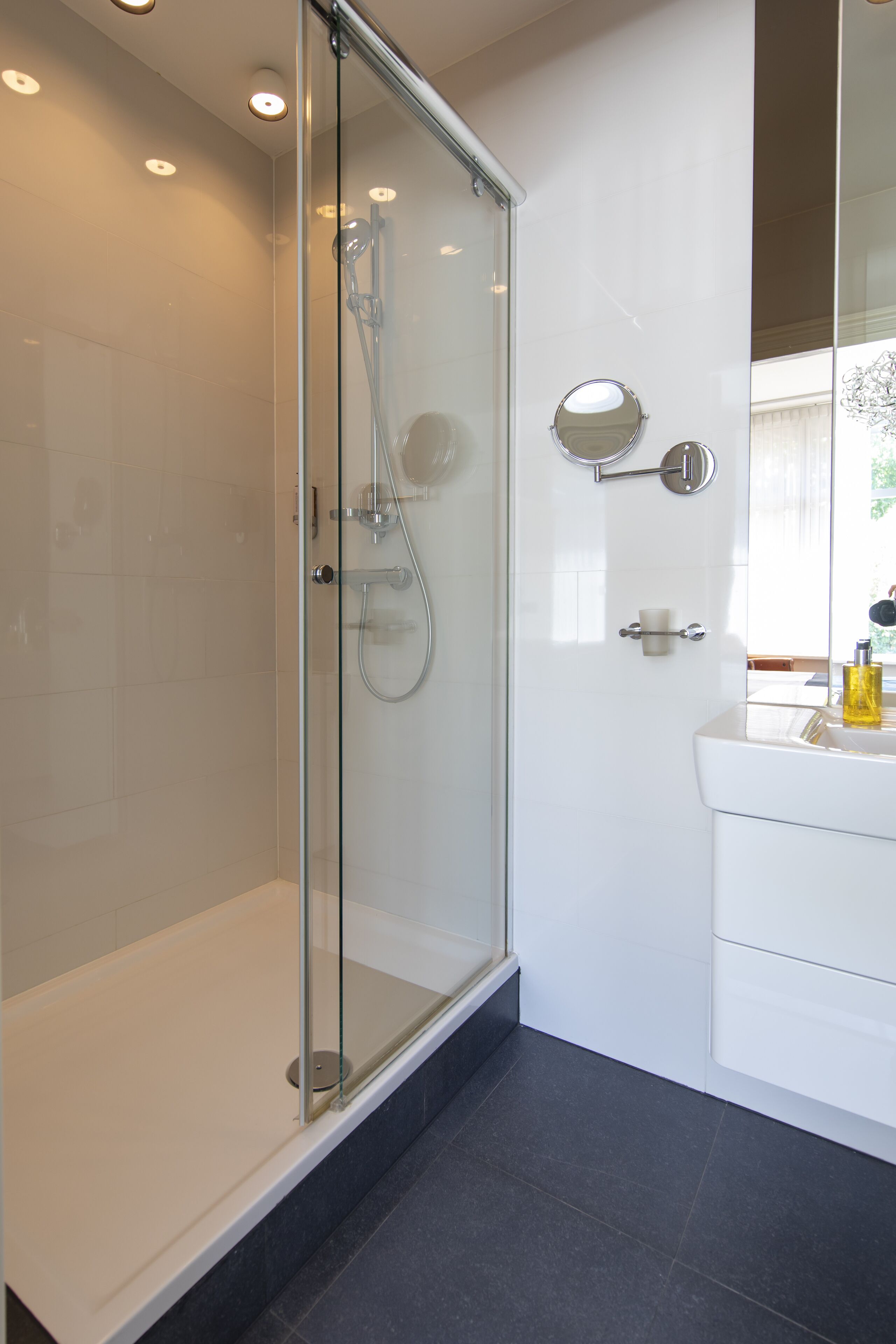 Une salle de bain moderne avec une douche à parois de verre, des carreaux blancs et un grand miroir.