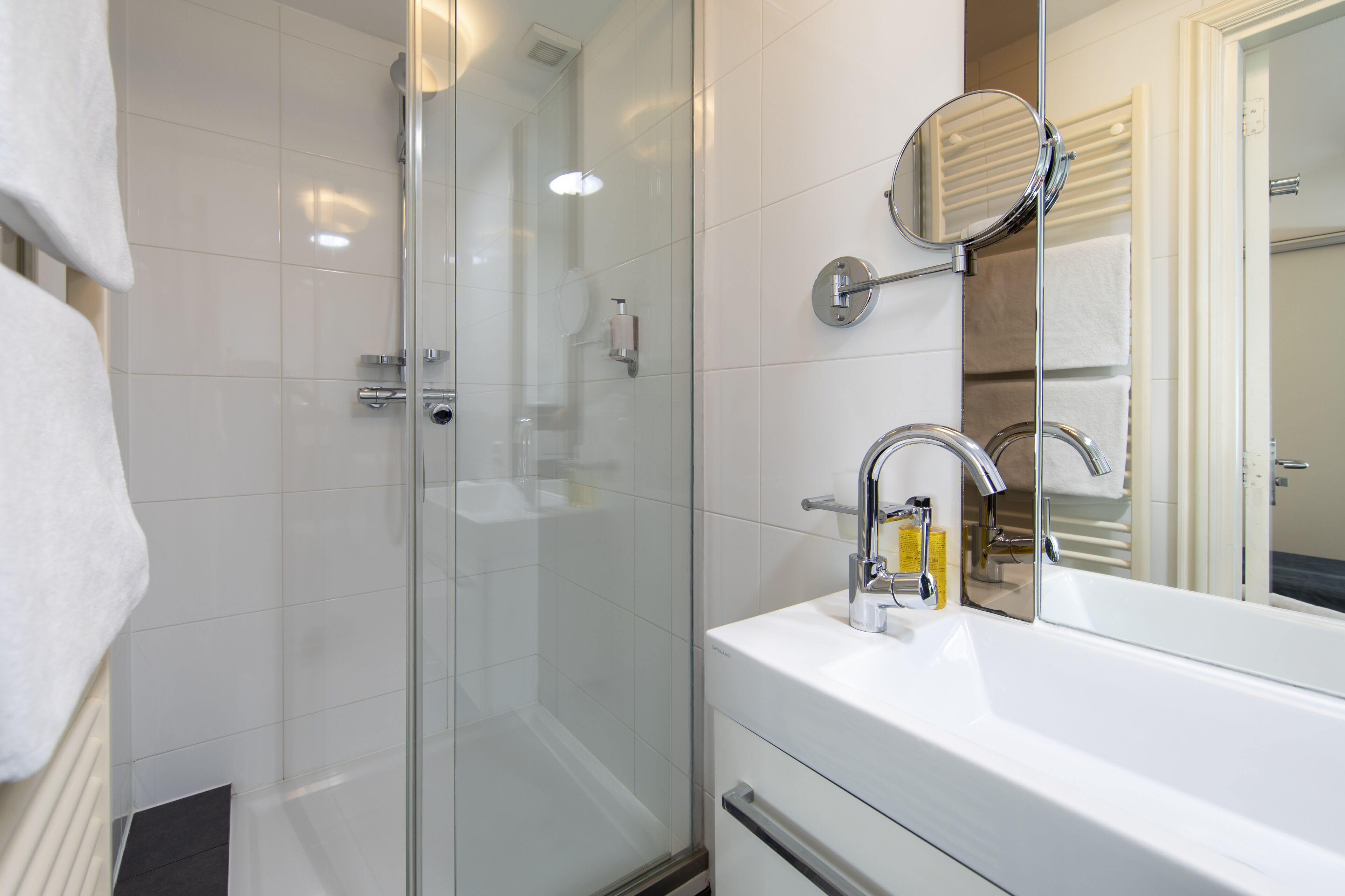 Une salle de bain moderne avec une douche à parois de verre, un lavabo blanc avec un miroir et un porte-serviettes.