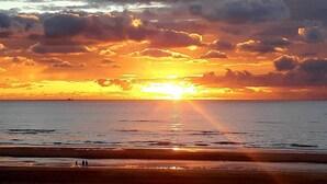 A beach with a sunset, calm sea, and a few people walking.