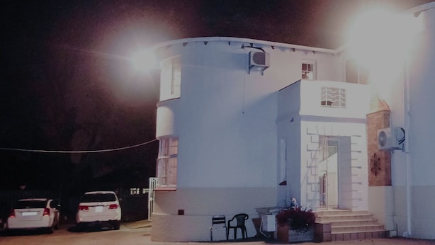 A white building with a central staircase, a door, and a window. There are two cars parked in front. - LTN Lodge (Johannesburg)