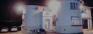 A white building with a central staircase, a door, and a window. There are two cars parked in front.