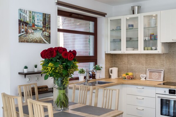 A modern kitchen with white cabinets, a wooden dining table, and a vase of red roses.