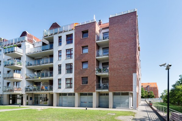 A multi-story residential building with balconies, a central entrance, and a paved walkway.