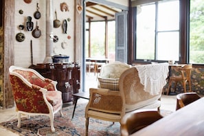 A room with a red upholstered chair, a wicker sofa, and a patterned rug.