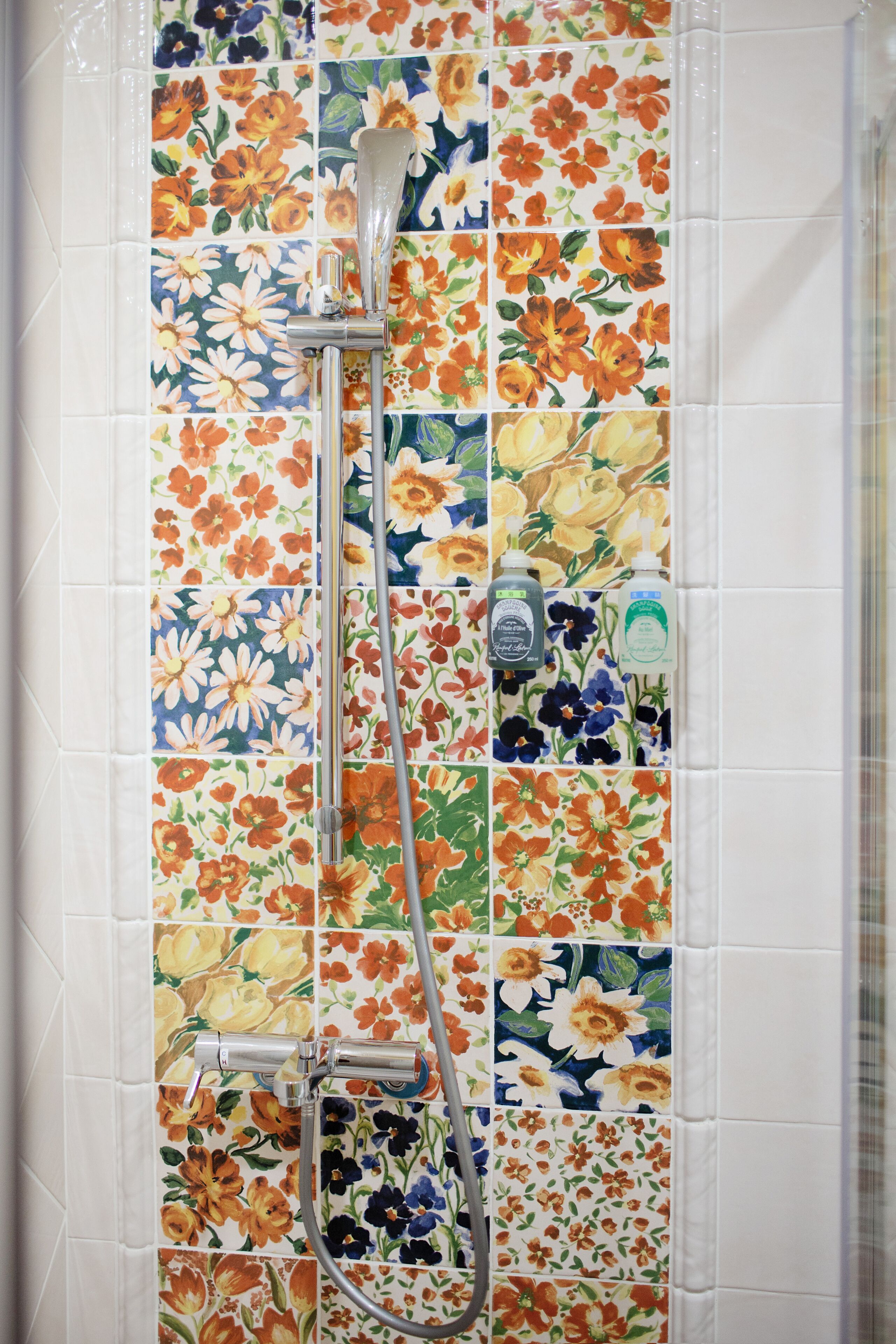 A shower with a floral tile backsplash and a handheld showerhead.