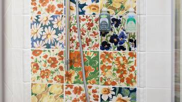 A shower with a floral tile backsplash and a handheld showerhead.