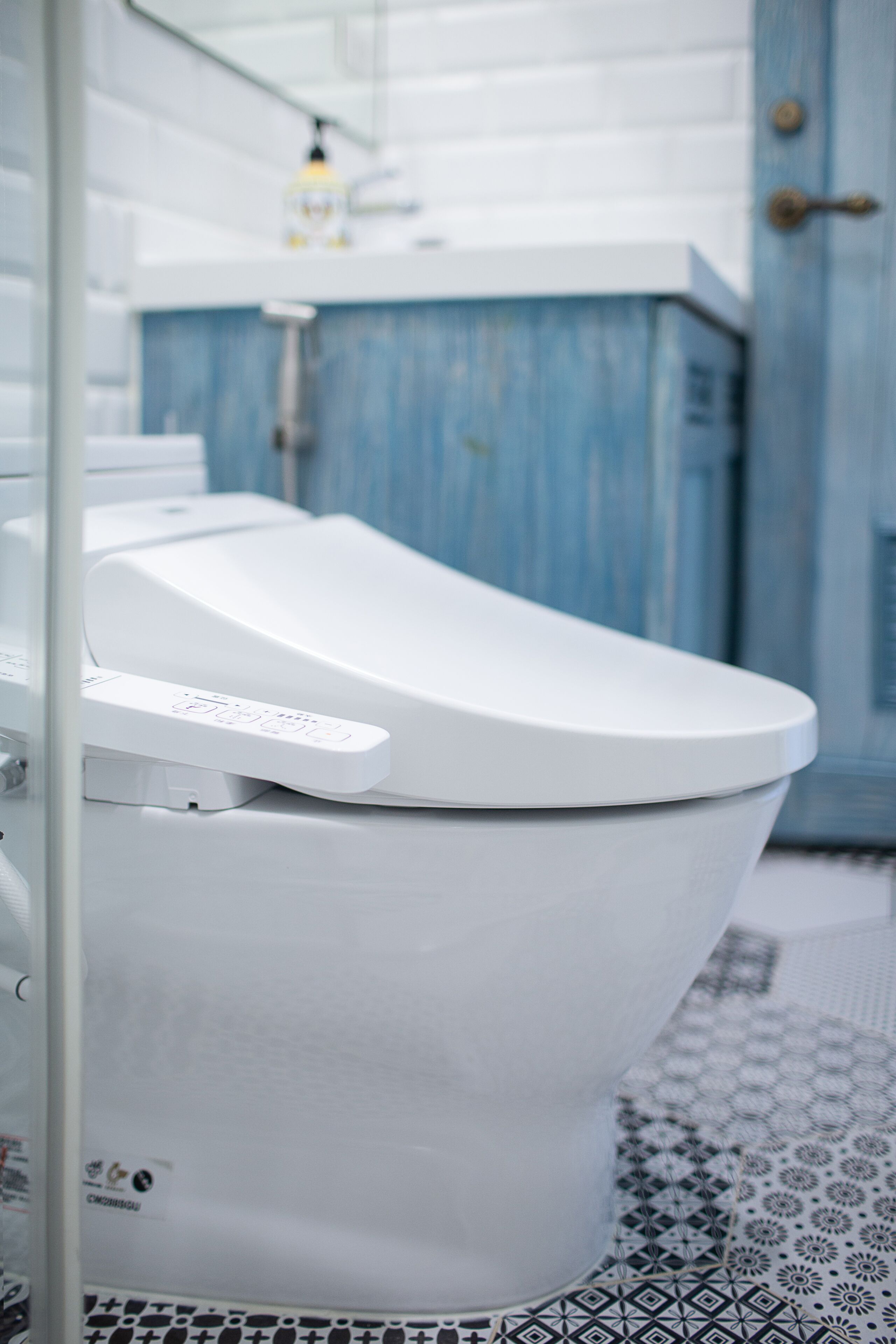 A modern toilet with a control panel, a blue cabinet in the background, and a patterned floor.