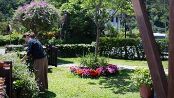 A garden with a variety of plants and flowers, a wooden bench, and a person tending to the plants.
