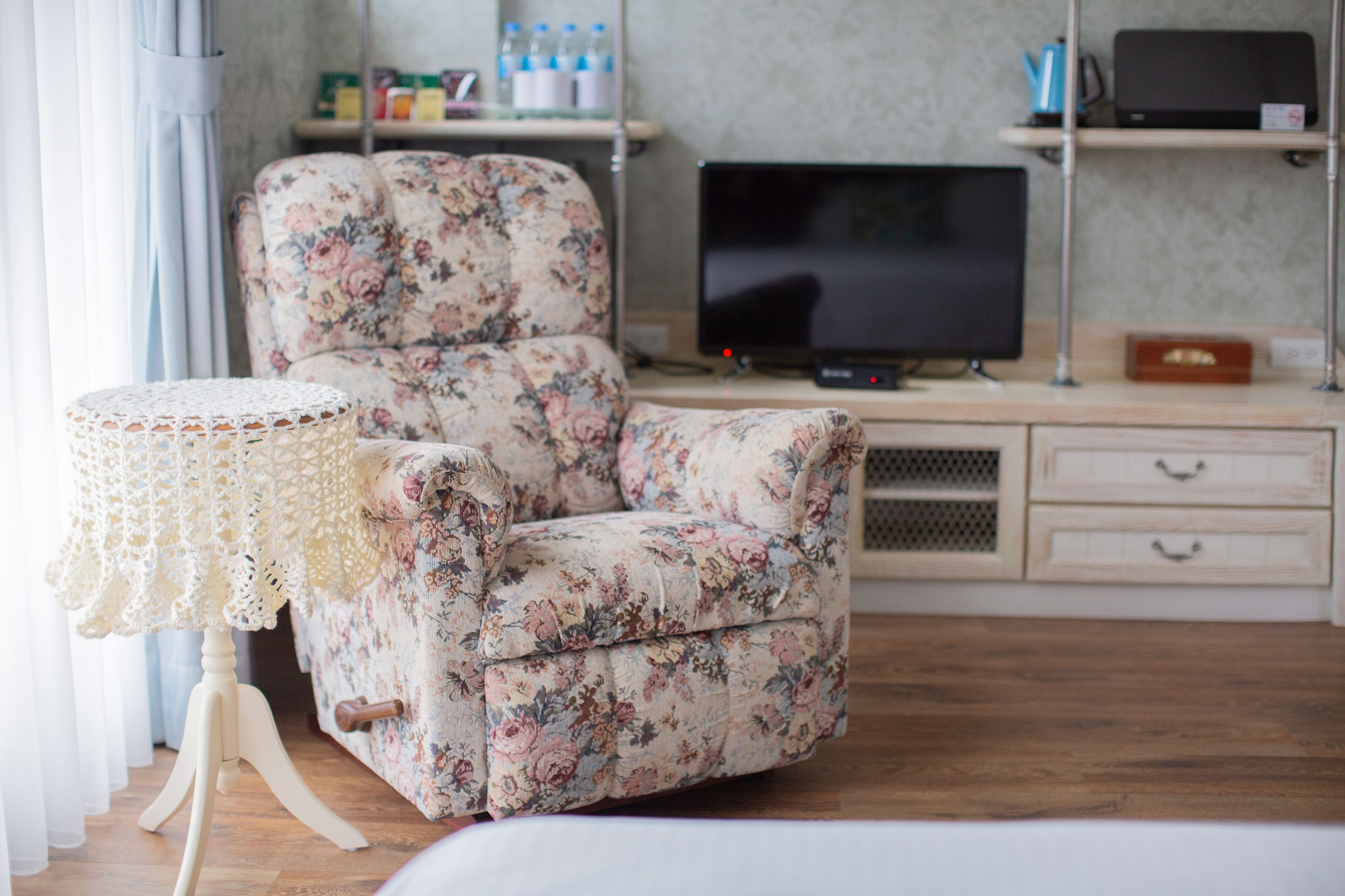 A living room with a floral sofa, a television, and a small table with a lace cover.