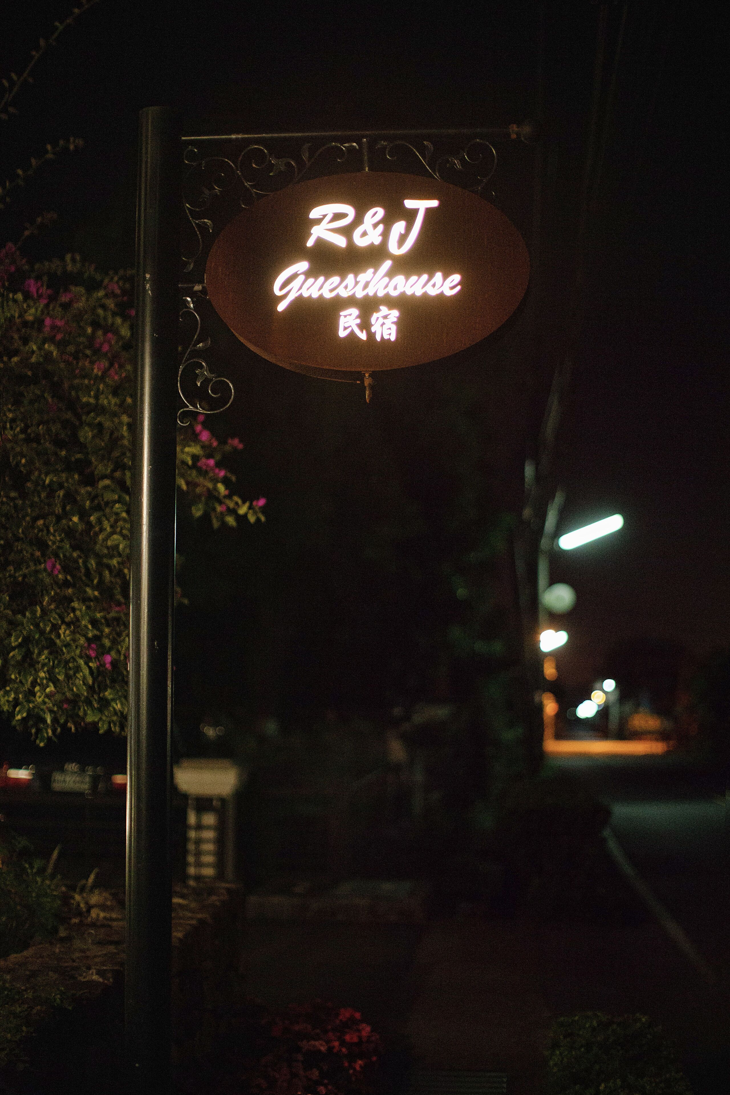 A neon sign for "R&J Guesthouse" in a dark outdoor setting.