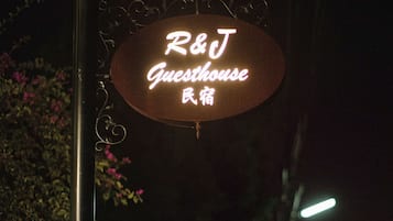 A neon sign for "R&J Guesthouse" in a dark outdoor setting.